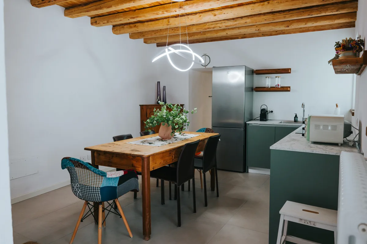 Il tavolo in legno e la cucina verde salvia sotto le travi a vista
